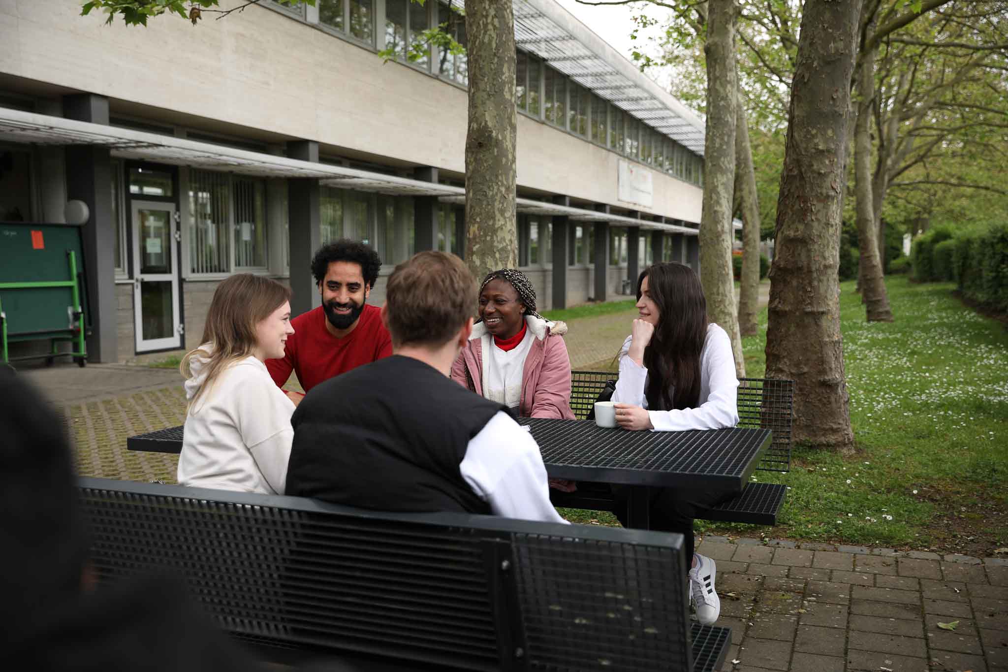 Studierende machen Pause an einem Tisch vor der Hochschule