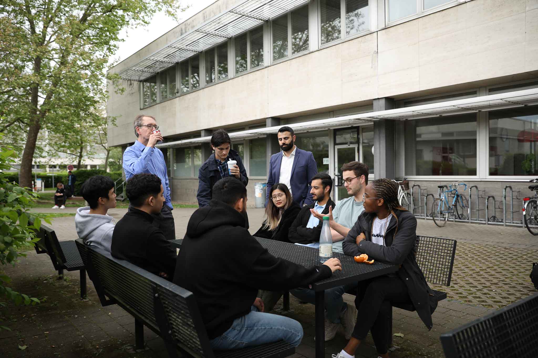 Studierende und ein Professor am Tisch vor der Hochschule
